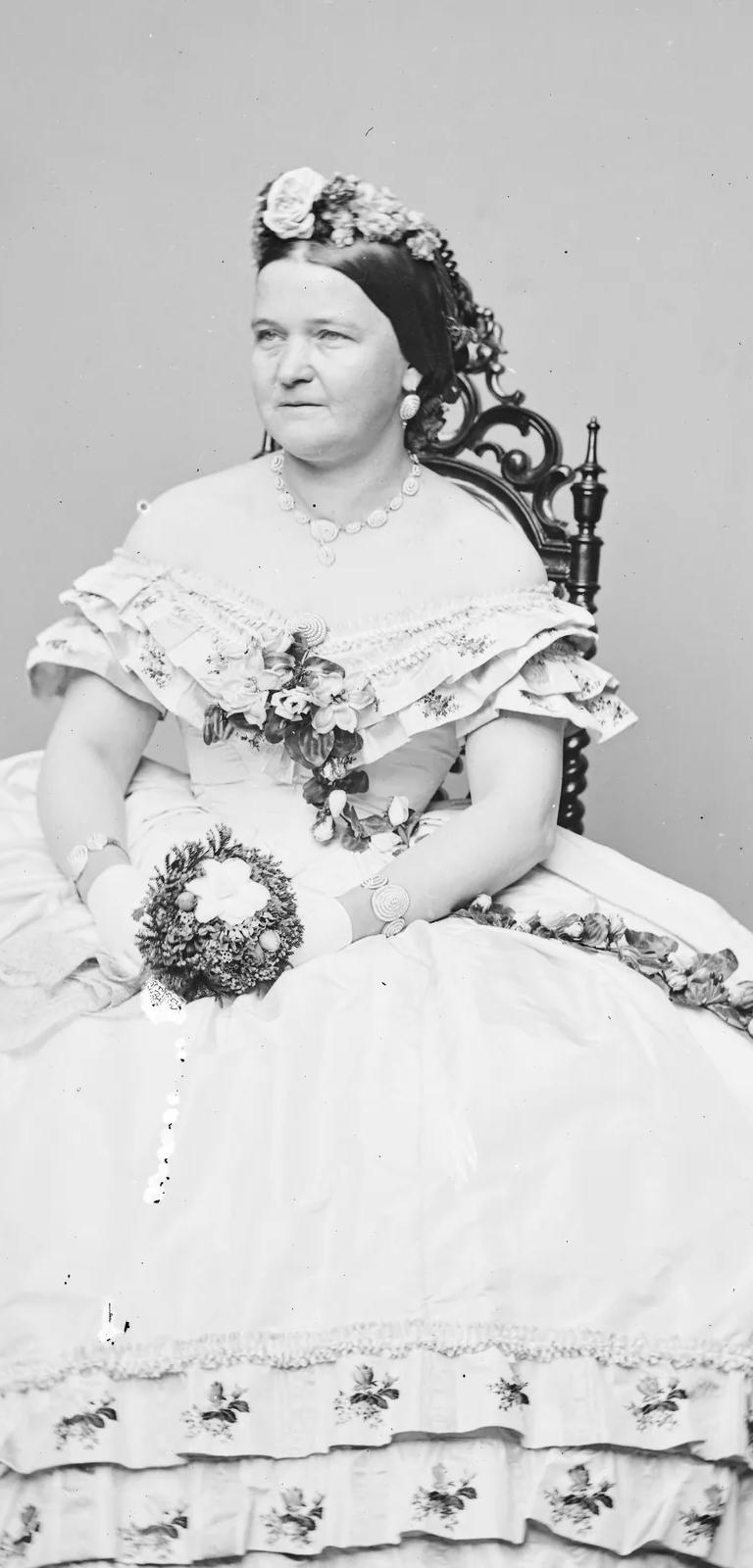 Black-and-white Mathew Brady studio portrait of a woman in a dress holding flowers