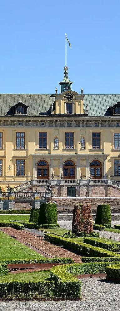 Yellow Baroque facade of Drottningholm Palace behind the clipped hedges of its formal Baroque garden