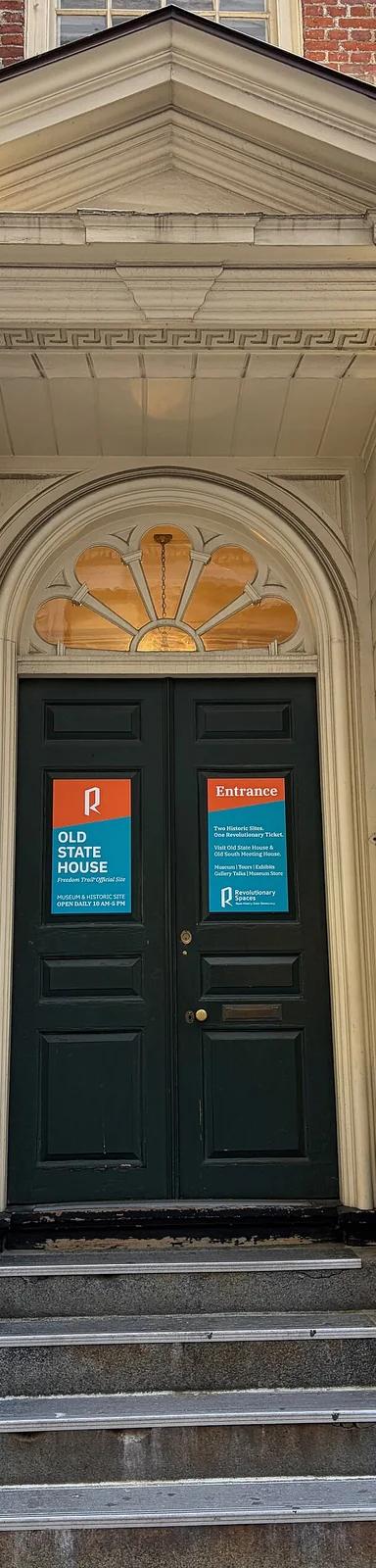 The brick facade and entrance of the 1713 Old State House on Washington Street in downtown Boston, framed by modern office towers