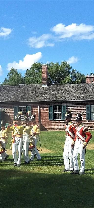 Fife-and-drum corps and redcoat re-enactors parade in front of a brick 1815 barracks at Fort York, Toronto